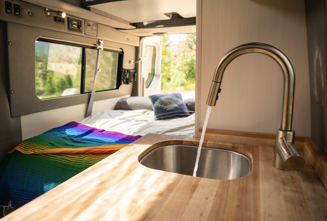 Inside this RV rental: a compact kitchen with running water, and a comfortable bed for road trip comfort. Van life ready!