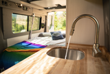 Inside this RV rental: a compact kitchen with running water, and a comfortable bed for road trip comfort. Van life ready!
