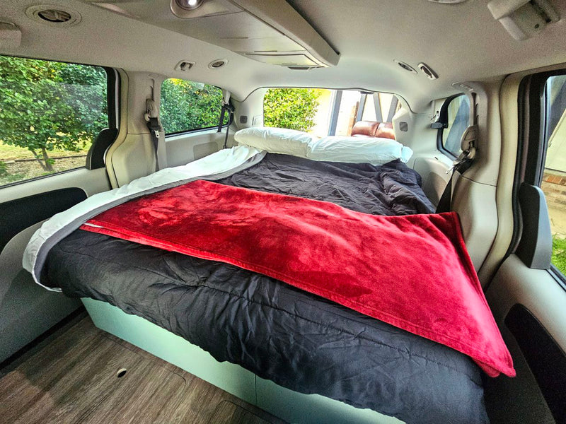 Inside an RV rental conversion: a cozy minivan bedroom with a black comforter, red blanket, and wood floor. — photo 14