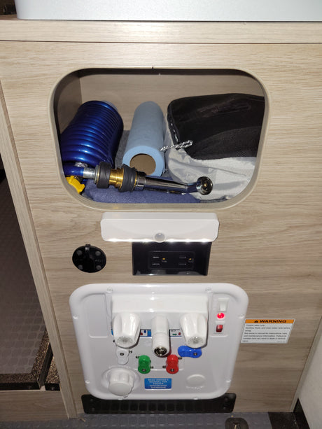 Essential RV rental utility panel: water valves, power, solar port, and storage with hose & shower sprayer. Includes safety warnings.