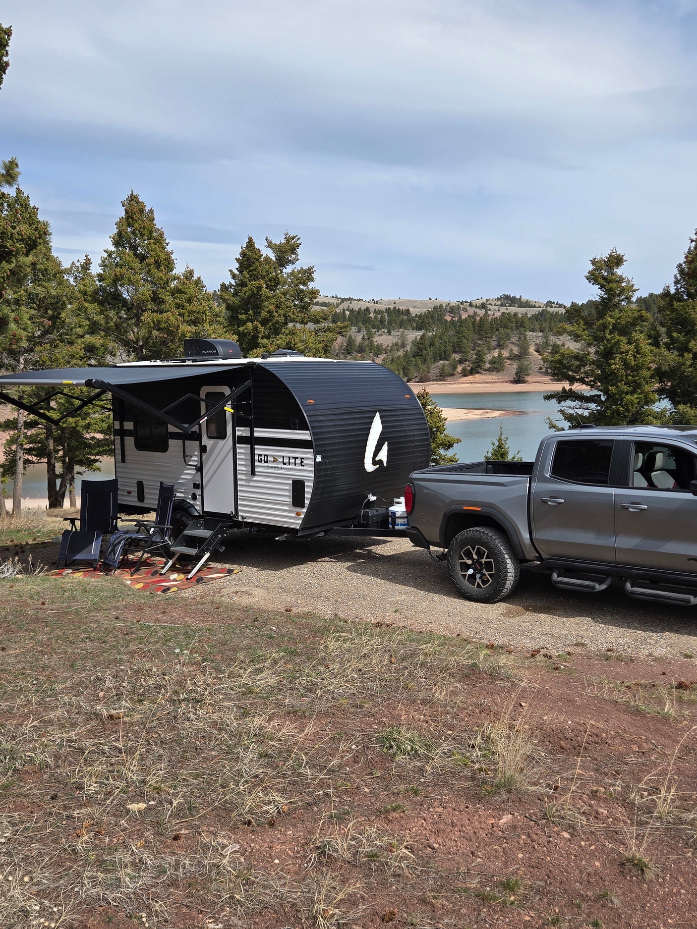 RV rental: Grey pickup tows a Go Lite travel trailer by a scenic lake campsite with trees and an extended awning.