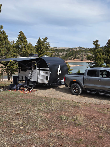 RV rental: Grey pickup tows a Go Lite travel trailer by a scenic lake campsite with trees and an extended awning.