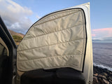 RV rental essential: A quilted window cover inside a camper van, framing scenic ocean and mountain views.