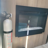 RV rental safety and comfort: a fire extinguisher mounted next to an electric fireplace with crystal media, set in a wood interior.
