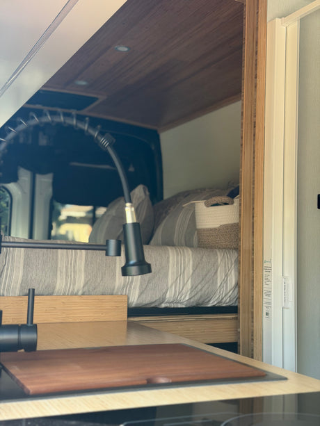 Compact rv rental interior showing a modern kitchen, cozy bed, and white space-saving shower door.