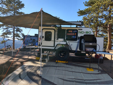 Compact RV rental at a scenic campsite, featuring an outdoor kitchen, extended awning, and comfortable outdoor living space.