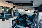 Inside an RV rental: a modern kitchenette with a sink and stovetop, a mini-fridge, front cabin seats, and overhead storage.