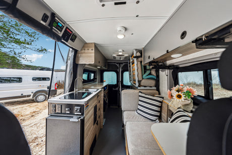 This RV rental showcases a modern camper van interior: kitchen with sink, comfy seating, overhead storage, and scenic outdoor views.