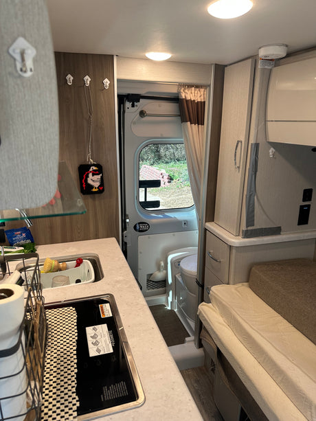 This RV rental interior reveals a compact galley kitchen (sink, Dometic stove), toilet in bathroom, and comfortable sleeping area.