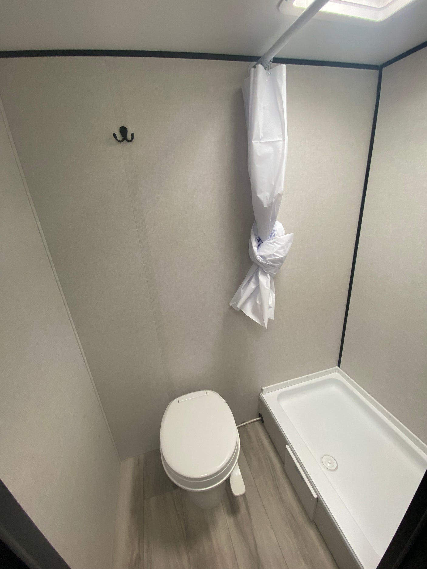 This RV rental bathroom features a compact design with a white toilet and a shower stall with a tied shower curtain.