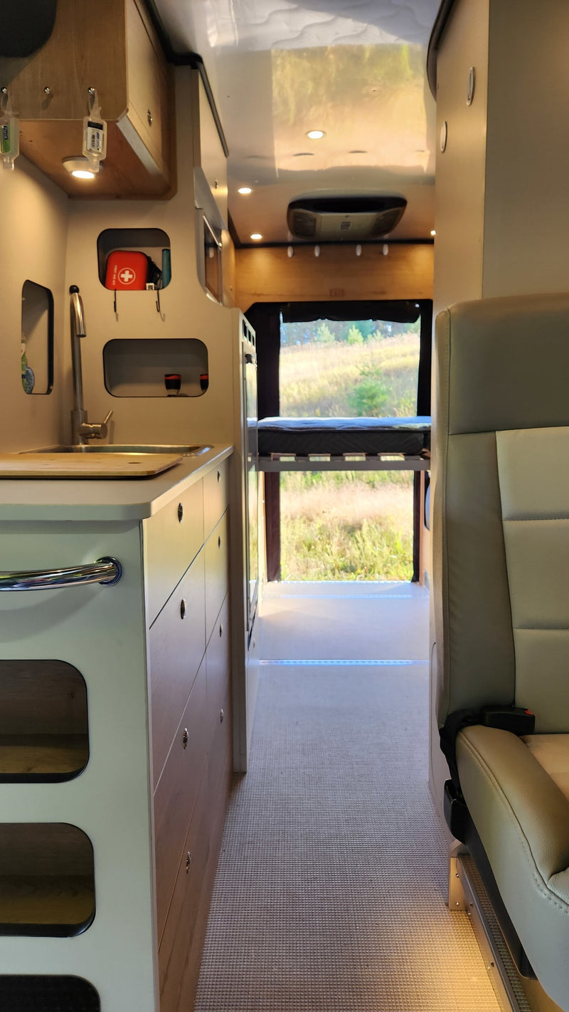 Inside this RV rental, see the compact kitchen, storage, and bed with an expansive outdoor view. — photo 17