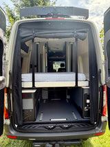 Inside a spacious RV rental camper van, rear doors open to reveal a comfortable elevated bed and functional storage.