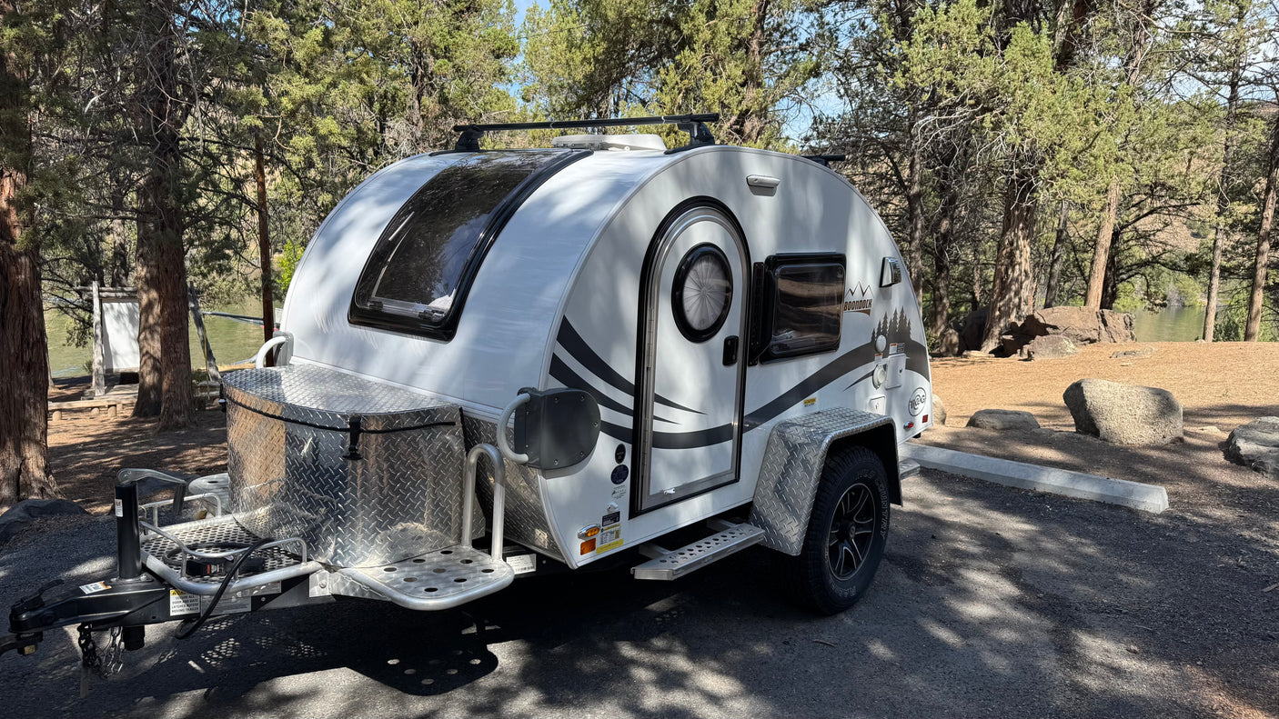 White nuCamp T@G Boondock teardrop **rv rental** parked at a wooded campsite, ideal for nature getaways by the water.