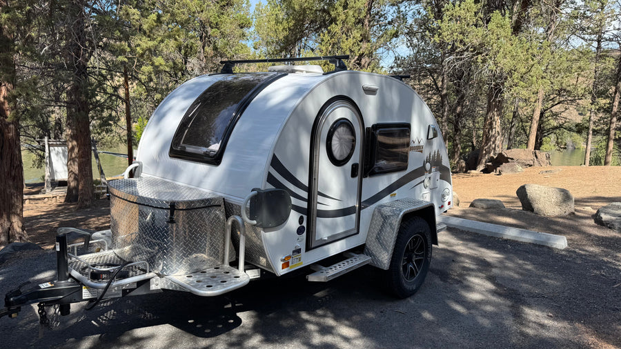 White nuCamp T@G Boondock teardrop **rv rental** parked at a wooded campsite, ideal for nature getaways by the water.