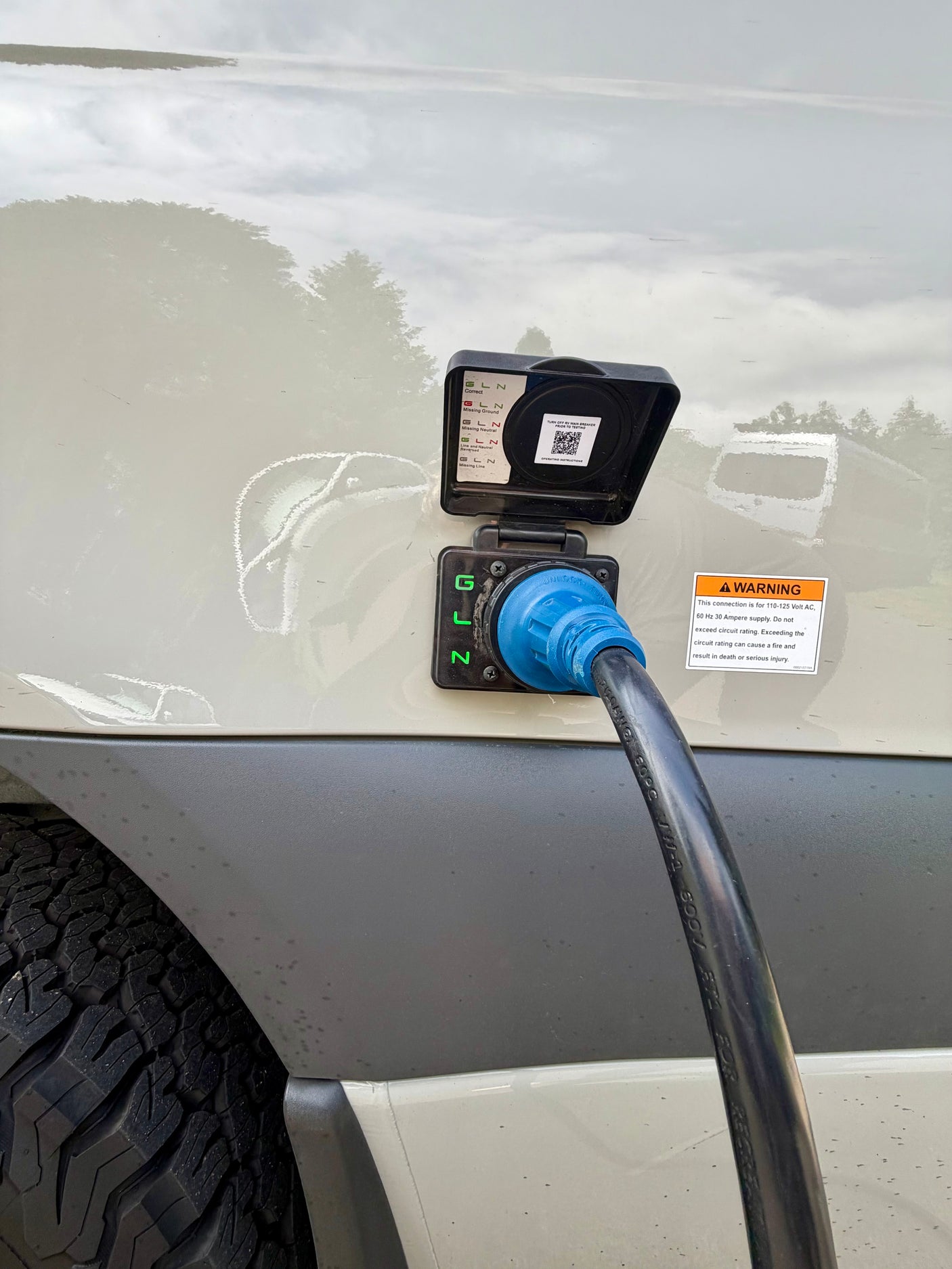 An RV rental is connected to shore power. A blue electrical inlet on the van shows diagnostic lights for a correct 110-125V, 30A connection.
