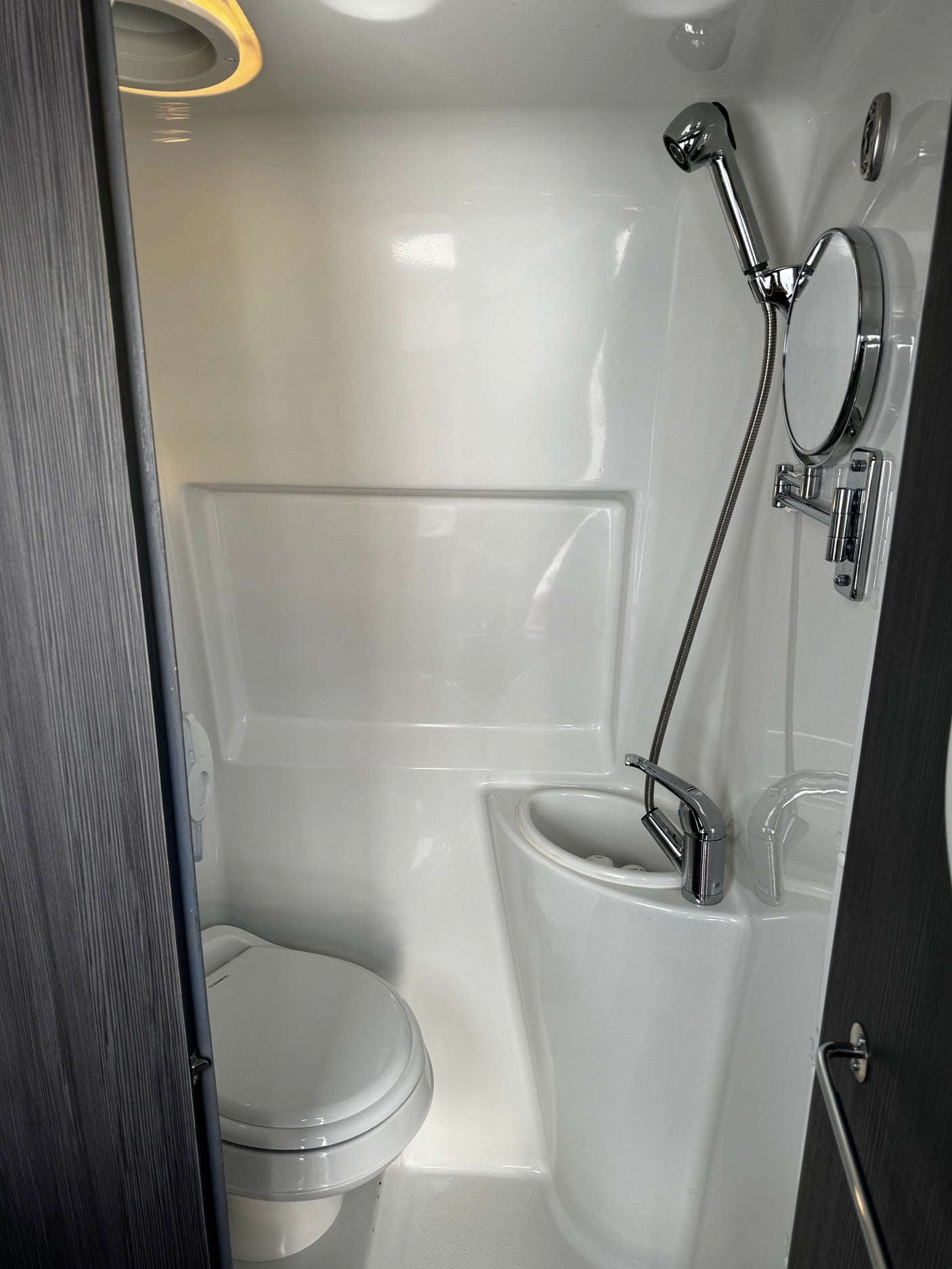RV rental's compact, all-in-one wet bath featuring a toilet, sink, shower, and mirror in a clean, white molded interior.