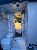 Inside an RV rental: a compact wet bath with shower and toilet, opening to a comfortable bedroom area.