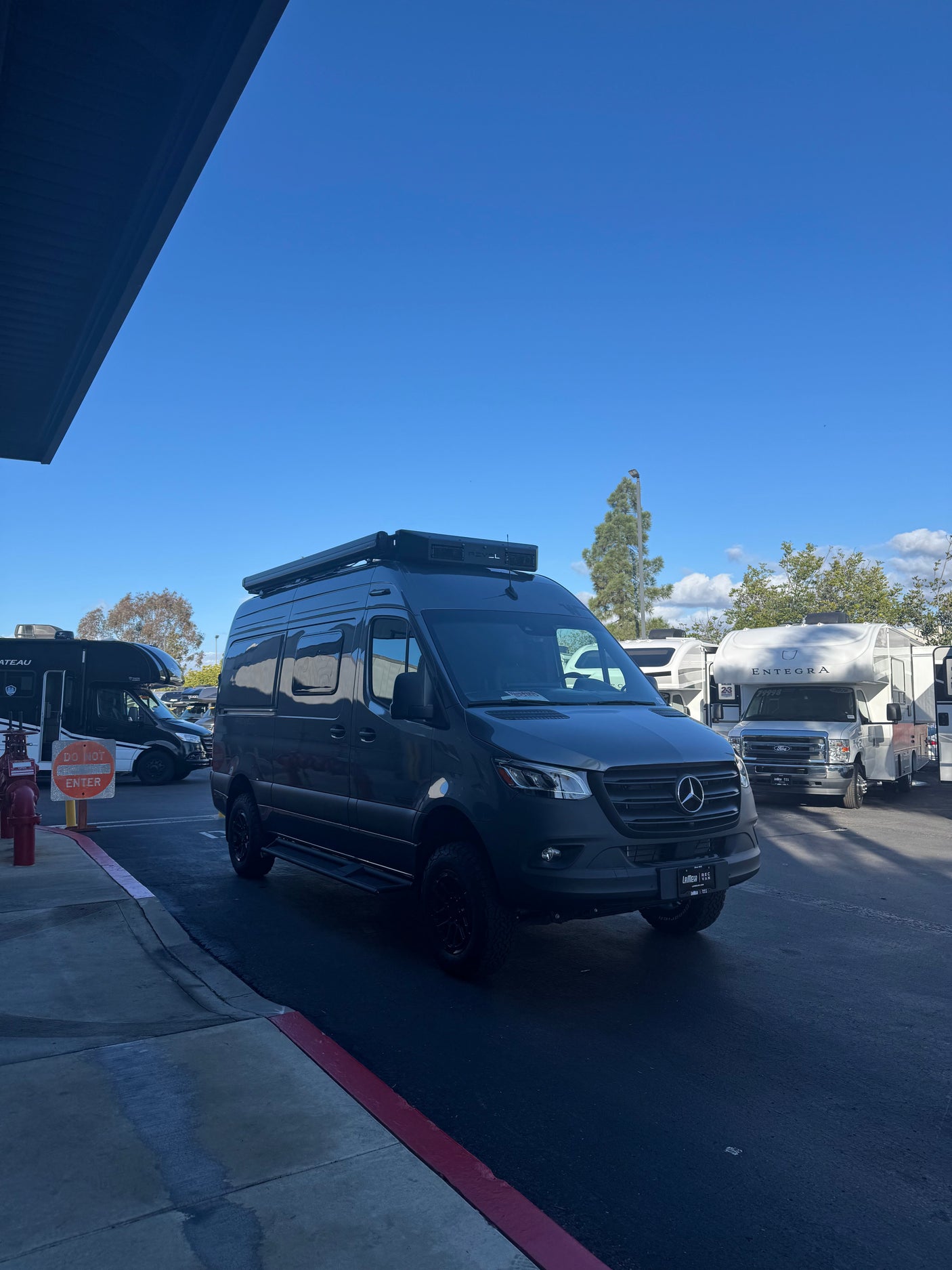 Dark grey Mercedes Sprinter van RV rental at an RV lot, with other RVs, a red fire hydrant, and a clear blue sky.