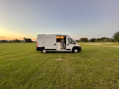 Freedom awaits with an RV rental! A person in their camper van, parked in a grassy field at sunset.