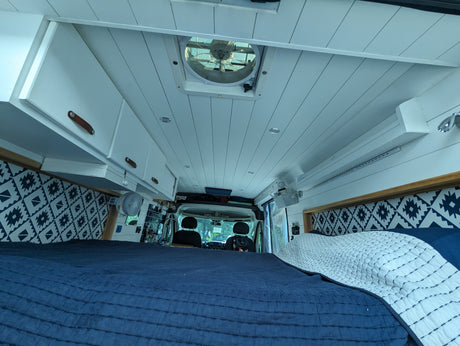 Experience van life in this rv rental. Features a spacious bed, overhead storage, & ceiling vent for comfort.