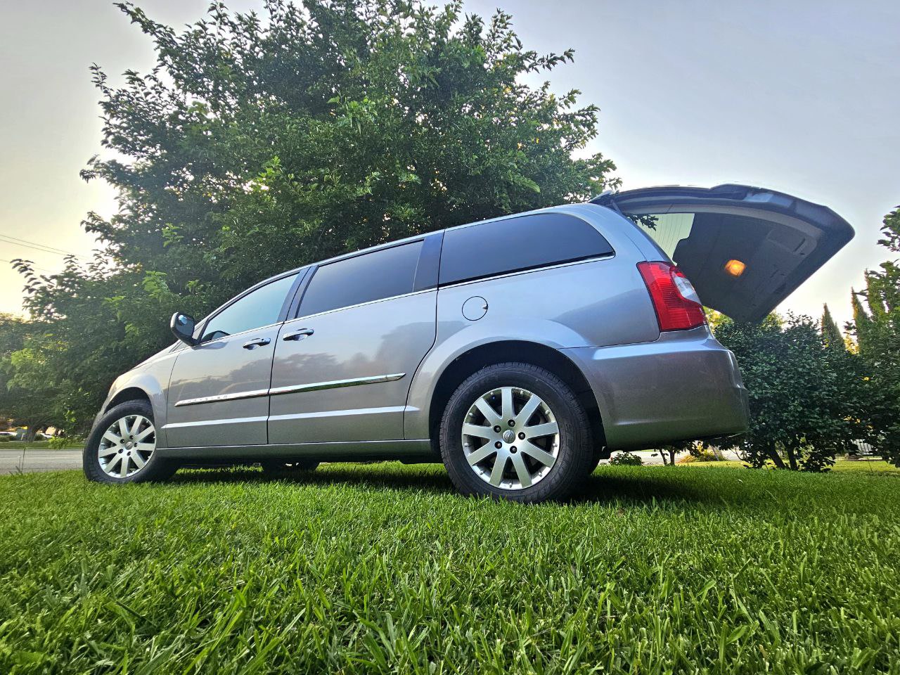 Explore the outdoors! This spacious minivan, perfect for your next RV rental trip, is ready with its rear hatch open on green grass. — photo 2