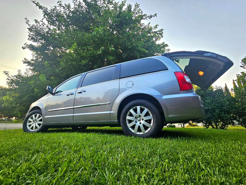 Explore the outdoors! This spacious minivan, perfect for your next RV rental trip, is ready with its rear hatch open on green grass. — photo 2