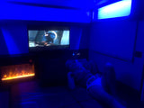 Unwind in a comfy rv rental! Person relaxes watching TV, beside a cozy electric fireplace & blue ambient lights.