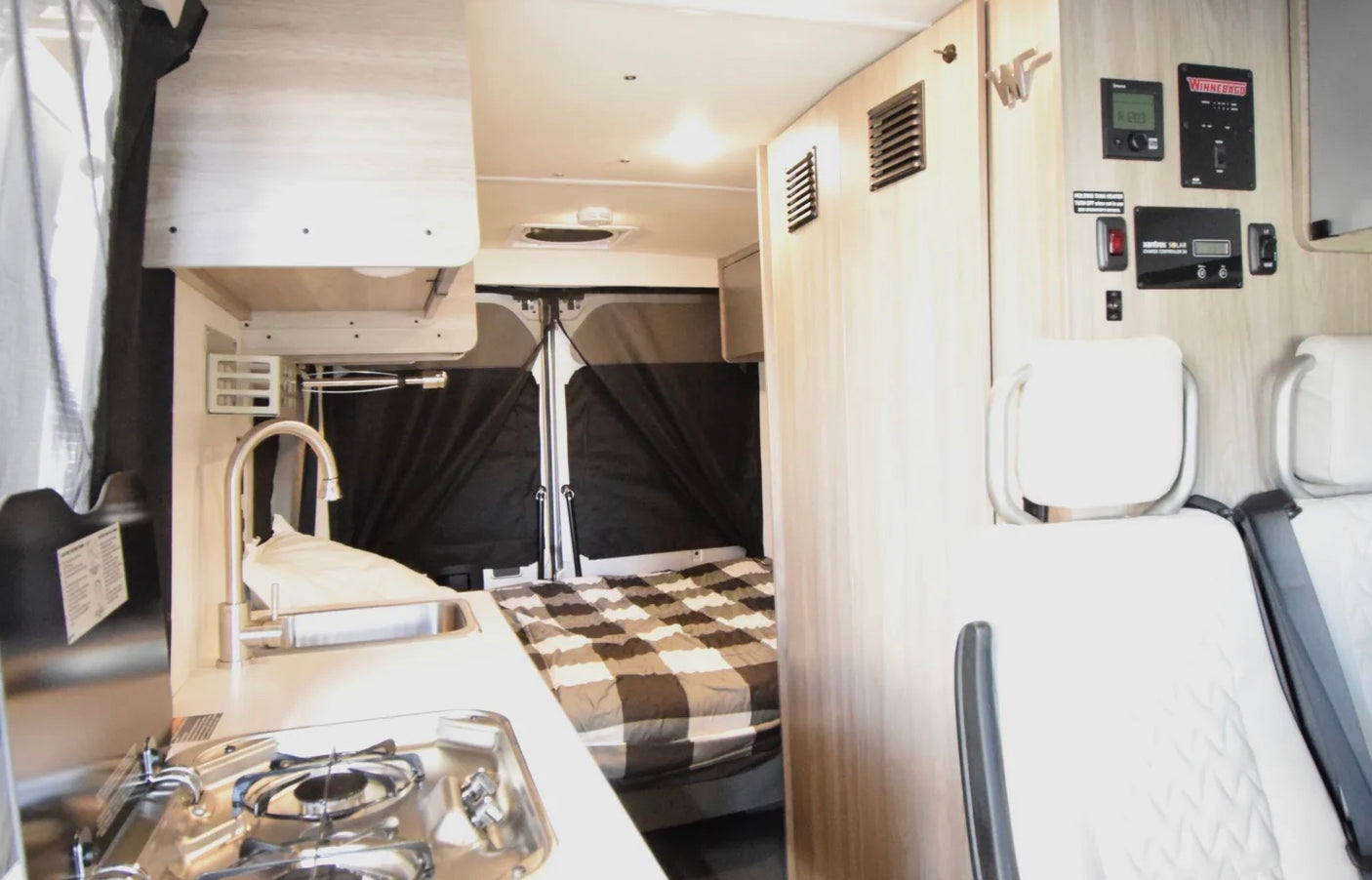 Inside this RV rental: a compact kitchenette with sink and stove, a cozy bed, and control panels for a comfortable journey.