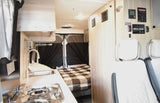Inside this RV rental: a compact kitchenette with sink and stove, a cozy bed, and control panels for a comfortable journey.
