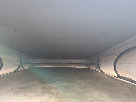 Interior of an RV rental pop-top camper: raised fabric roof, bed, and ceiling lights, providing a comfortable sleeping space.
