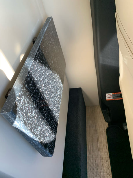 Inside an RV rental: dark speckled counter, light seating, and woven floor mat. Functional, compact vehicle interior.