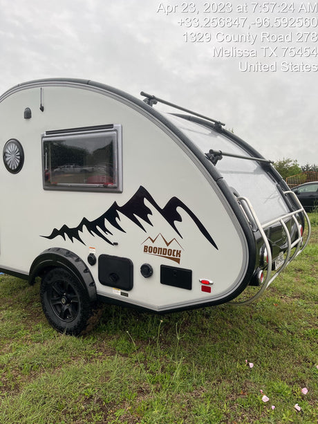 Explore the outdoors with this Boondock teardrop RV rental trailer. A rugged camper ready for adventure, parked on grass.