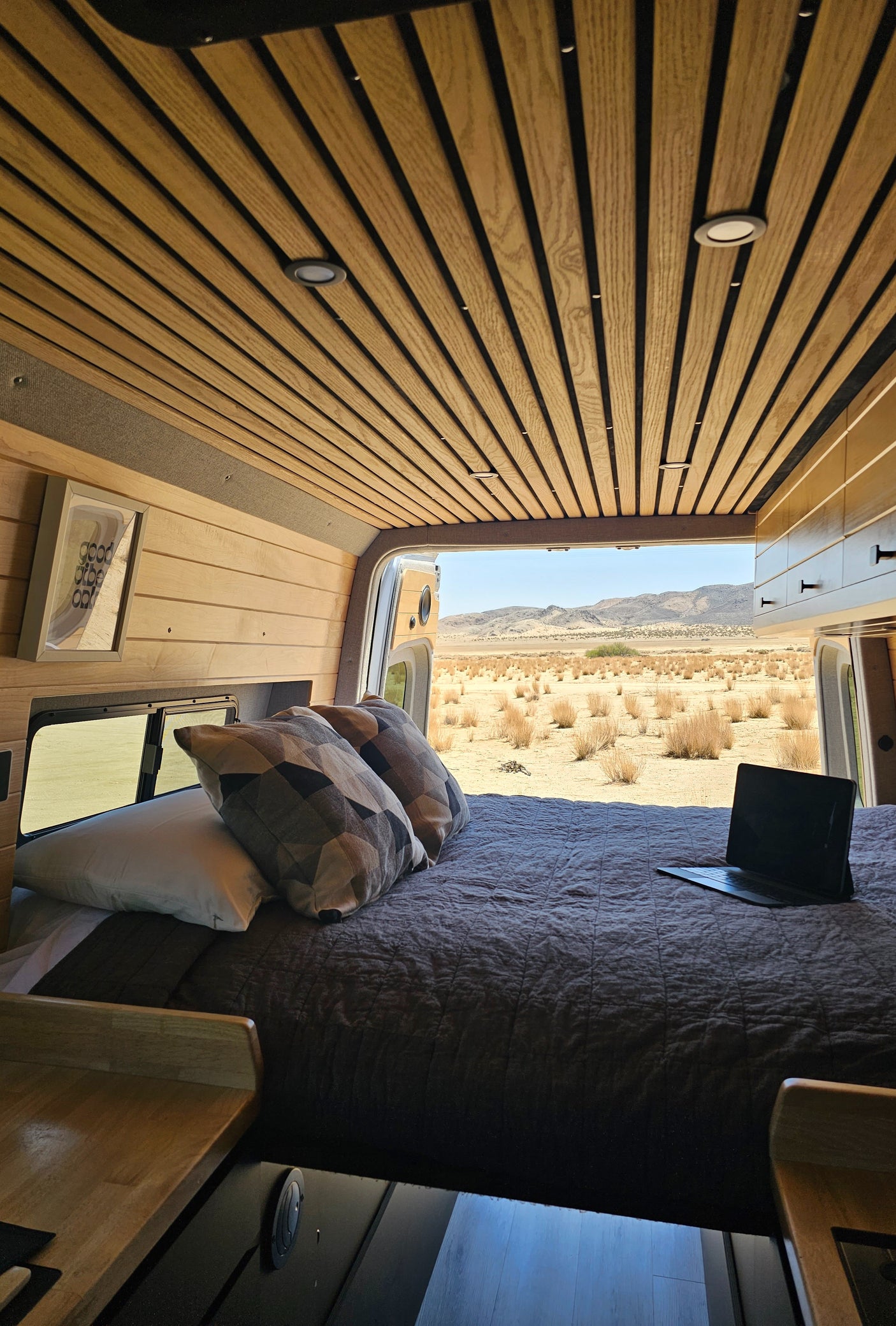 RV rental interior: a cozy bed, wood-slatted walls, and a vast desert mountain view outside.
