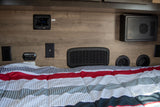 RV rental bedroom: Wall features Jensen audio, power outlets, CO detector, various vents, and a WFCO unit above a comfy bed.