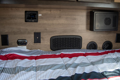 RV rental bedroom: Wall features Jensen audio, power outlets, CO detector, various vents, and a WFCO unit above a comfy bed.