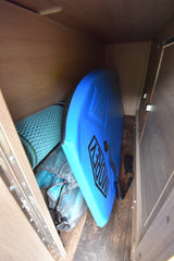 A blue Morey boogie board, rolled mat, and bag are neatly stored in an RV rental's compact interior storage compartment.