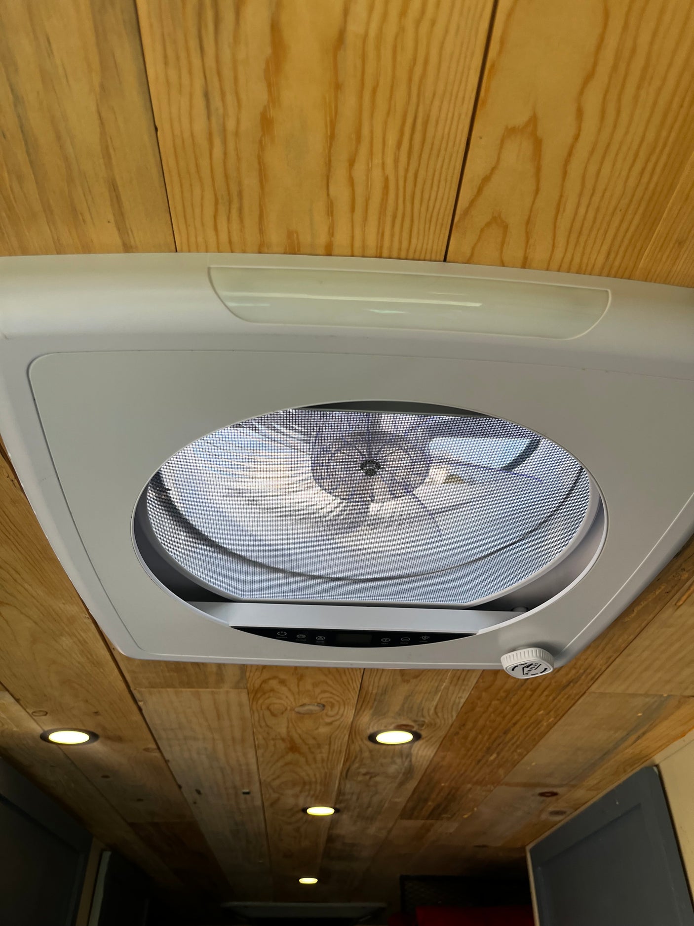Modern ceiling vent fan with mesh screen and controls set into a beautiful wooden ceiling with recessed lights in this RV rental.