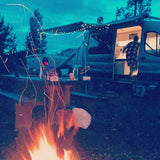 Cozy night camping with an RV rental! A person exits the lit campervan under string lights, beside a warm campfire & picnic table.