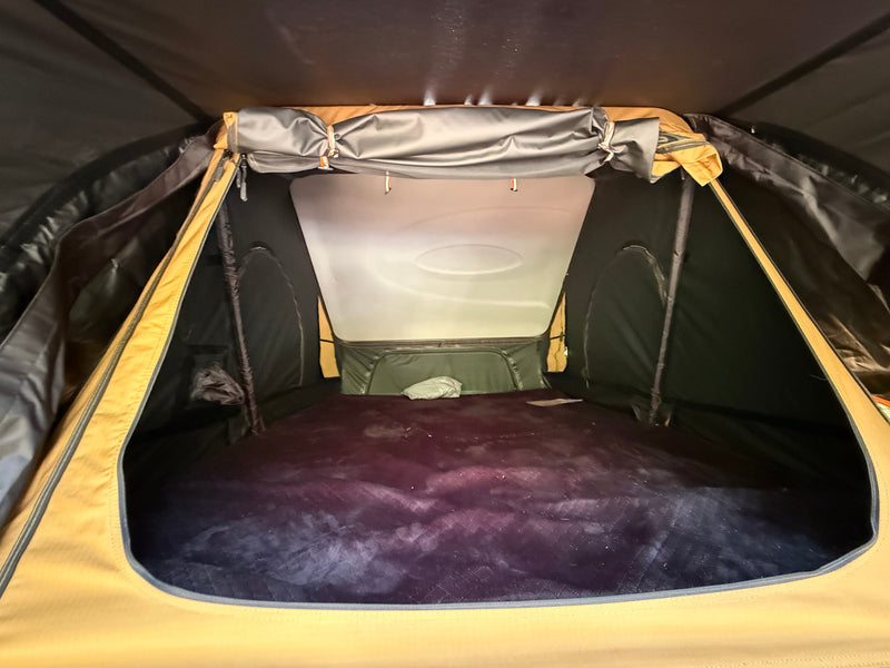 View inside an RV rental rooftop tent, showing a dark padded sleeping area, black walls, and a light-colored ceiling. — photo 3