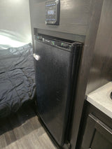 RV rental interior: Compact fridge with child lock, Jensen control panel above, and a grey quilted bed in the RV bedroom.