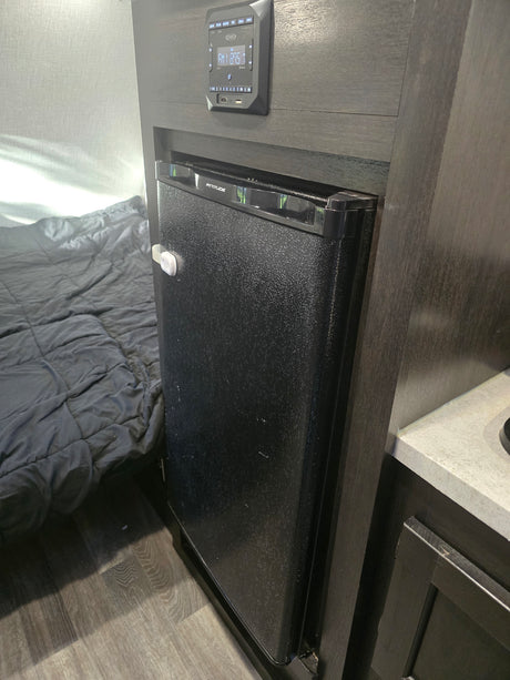 RV rental interior: Compact fridge with child lock, Jensen control panel above, and a grey quilted bed in the RV bedroom.