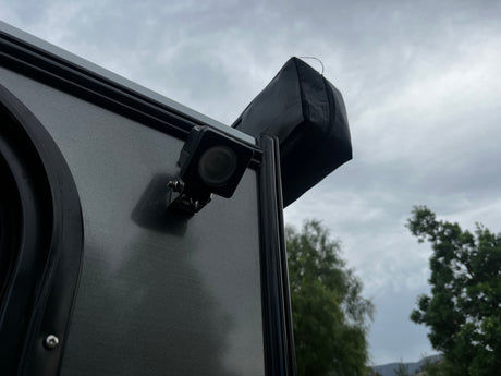 Cloudy sky over an RV rental. Side view shows a dark gray panel, black LED light, and a black zippered awning cover on the roof.