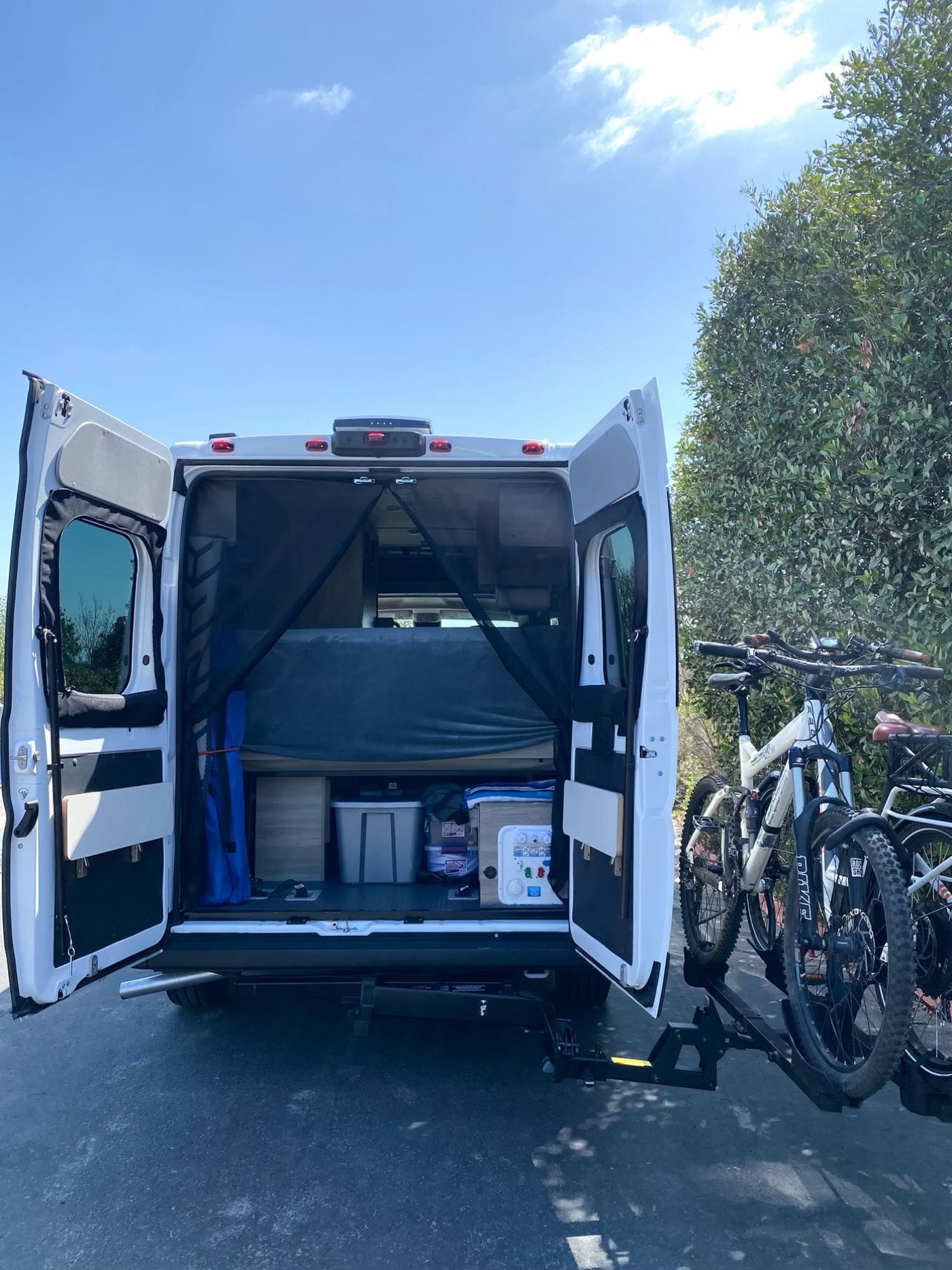 Spacious RV rental with rear doors open, showing ample storage & a bed, plus bikes on the hitch rack for outdoor trips. — photo 19