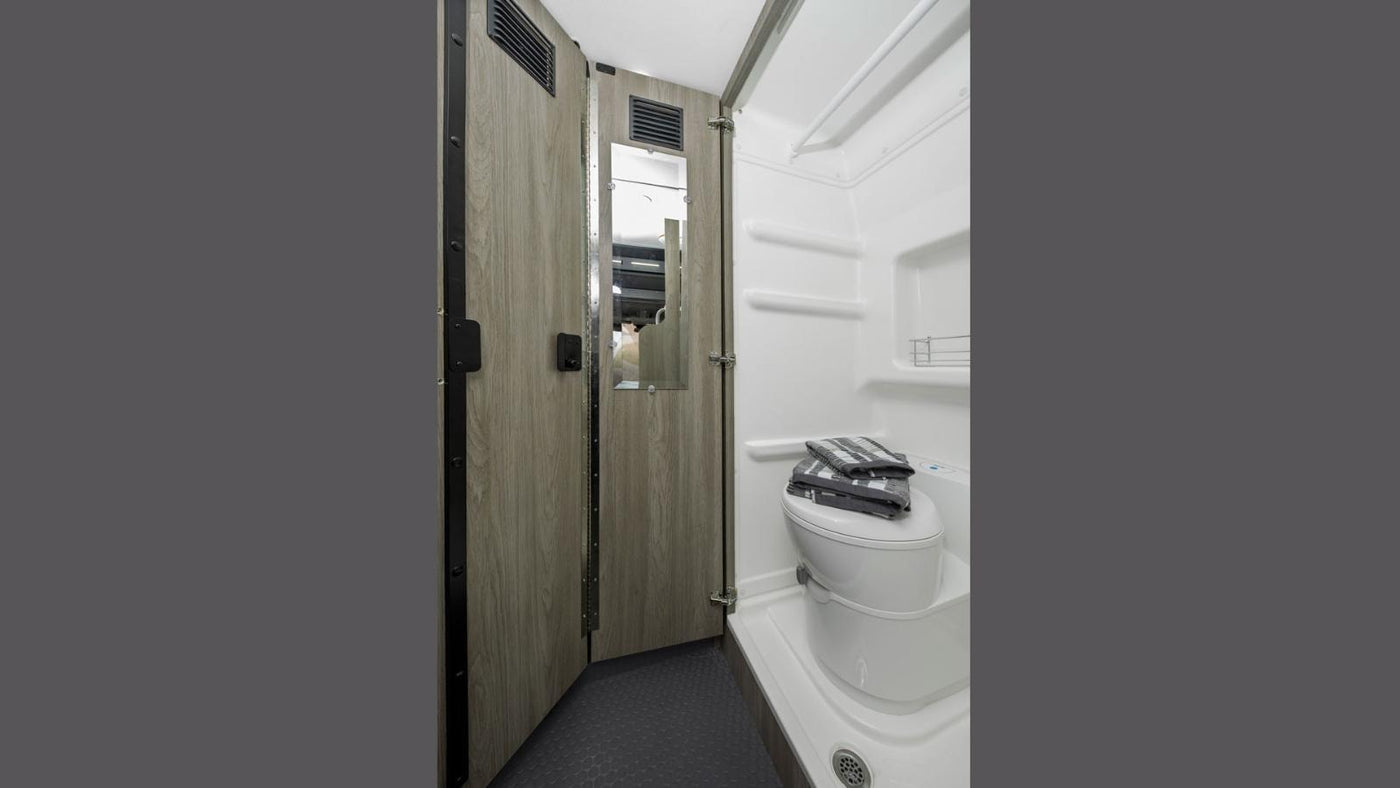 Compact RV rental wet bath featuring a toilet with towels, shower area, wood-look walls, and a mirror. — photo 12
