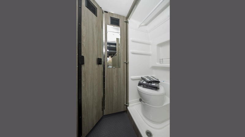 Compact RV rental wet bath featuring a toilet with towels, shower area, wood-look walls, and a mirror. — photo 12