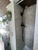 RV rental: Stylish interior showcasing a herringbone tiled shower with black and gold fixtures, and cozy bench seating.