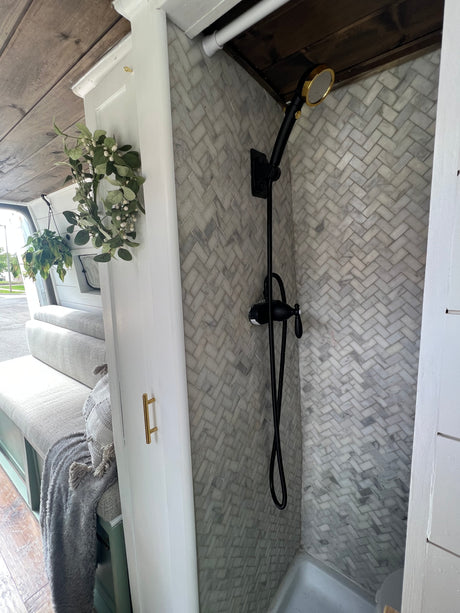 RV rental: Stylish interior showcasing a herringbone tiled shower with black and gold fixtures, and cozy bench seating.