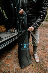 A person extracts a black Dragon Fly Tarps bag from an RV rental, preparing for an outdoor camping adventure.
