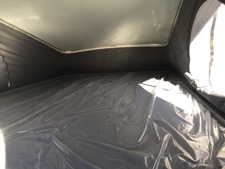RV rental: Inside a pop-top camper featuring a light ceiling, dark fabric walls, and a crinkled plastic-covered floor.