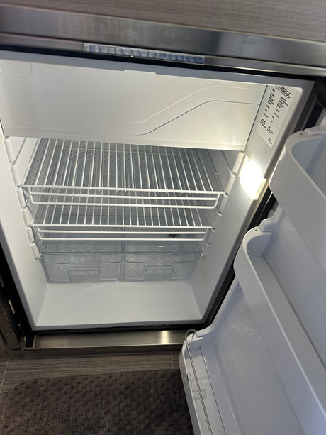 The clean, empty refrigerator interior of an rv rental, featuring wire shelves and clear bottom bins, ready for use.